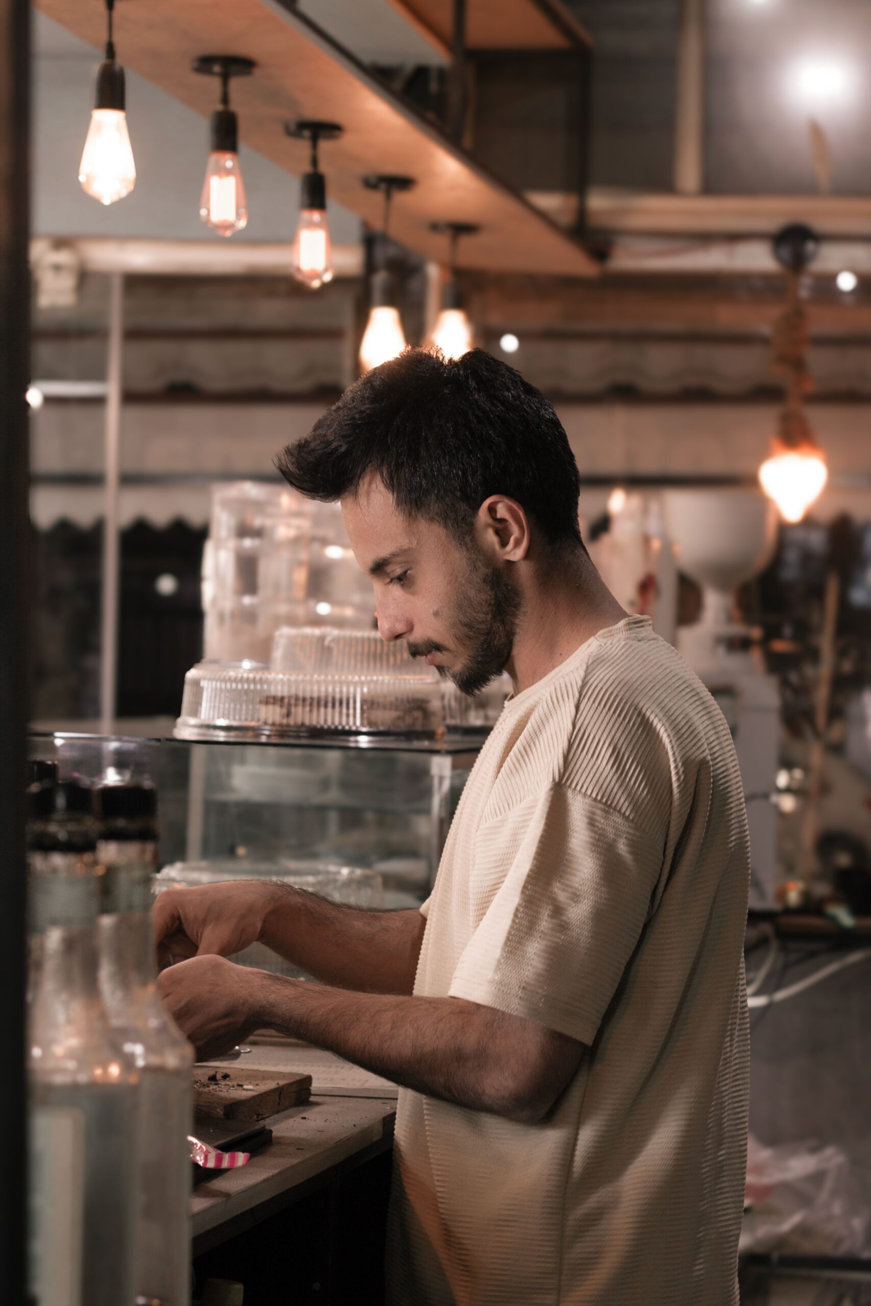 A barista prepares beverages in a warm-lit cafe in Kermanshah, Iran.