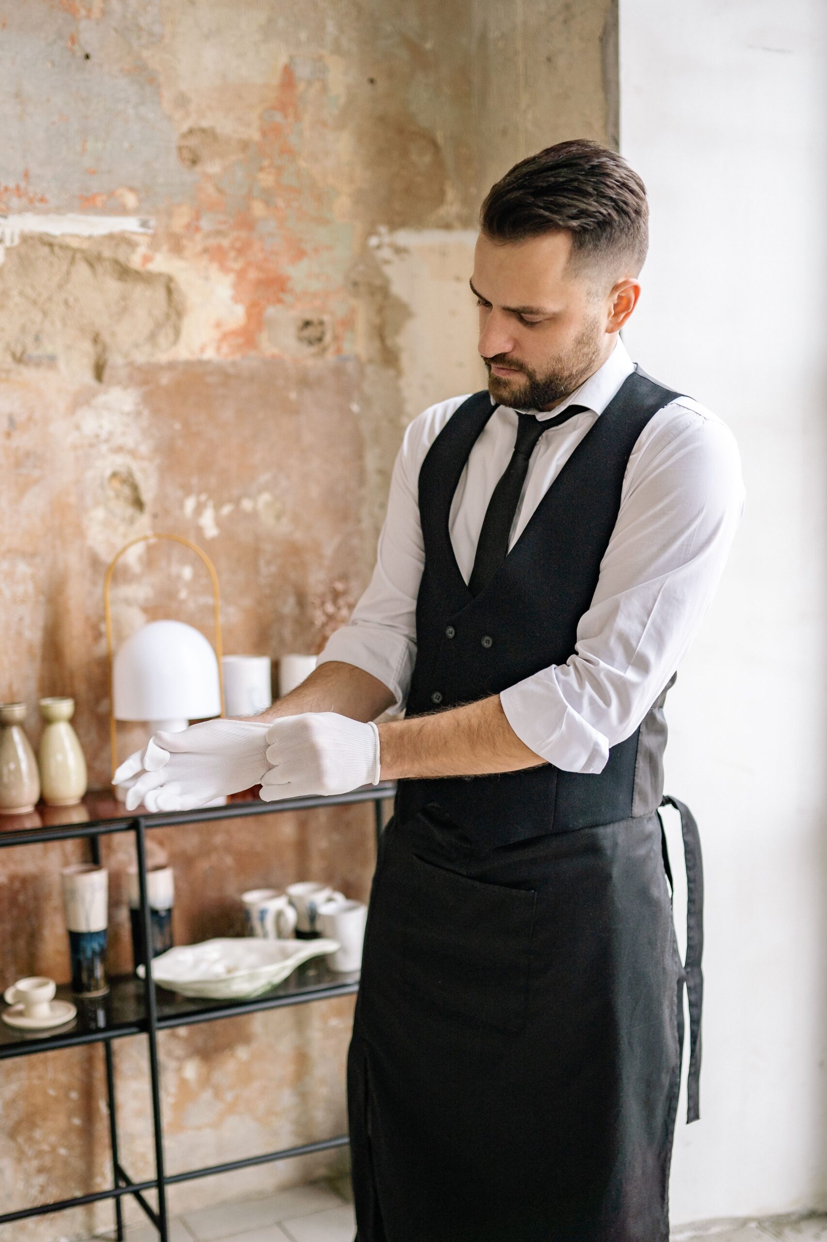 Elegant waiter adjusting gloves in rustic cafe interior, ready to serve guests.